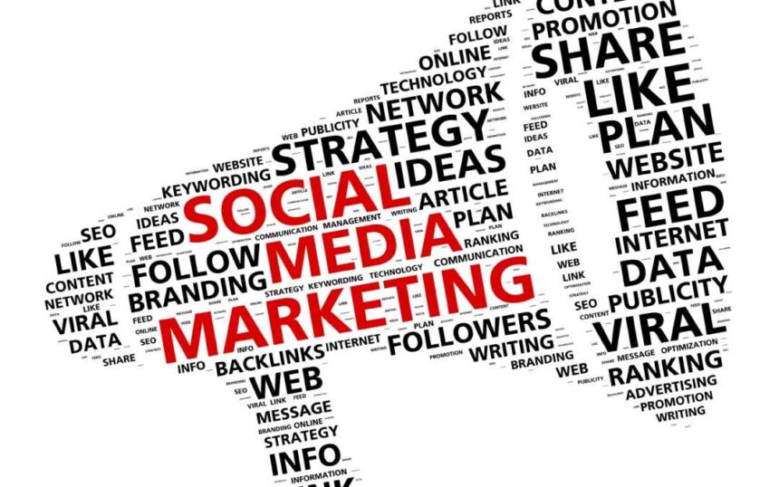 A marketer writing in a social media marketing plan notebook with a laptop and smartphone on the desk.