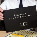 A person at a clean, well-lit desk with a notebook labeled "My Financial Plan," a calculator, a laptop showing a budgeting tips spreadsheet, and a steaming mug of coffee, conveying a sense of calm control.