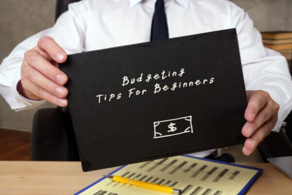 A person at a clean, well-lit desk with a notebook labeled "My Financial Plan," a calculator, a laptop showing a budgeting tips spreadsheet, and a steaming mug of coffee, conveying a sense of calm control.