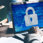 A graphic of a shield protecting a laptop from incoming digital threats like virus icons and hacker symbols, illustrating computer