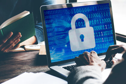 A graphic of a shield protecting a laptop from incoming digital threats like virus icons and hacker symbols, illustrating computer