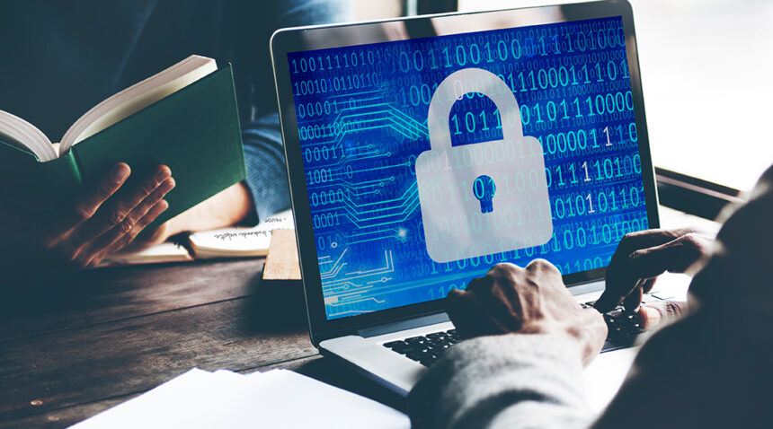 A graphic of a shield protecting a laptop from incoming digital threats like virus icons and hacker symbols, illustrating computer