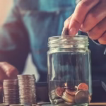 A person carefully placing a coin into a piggy bank, symbolizing the first step to save money on a low income.
